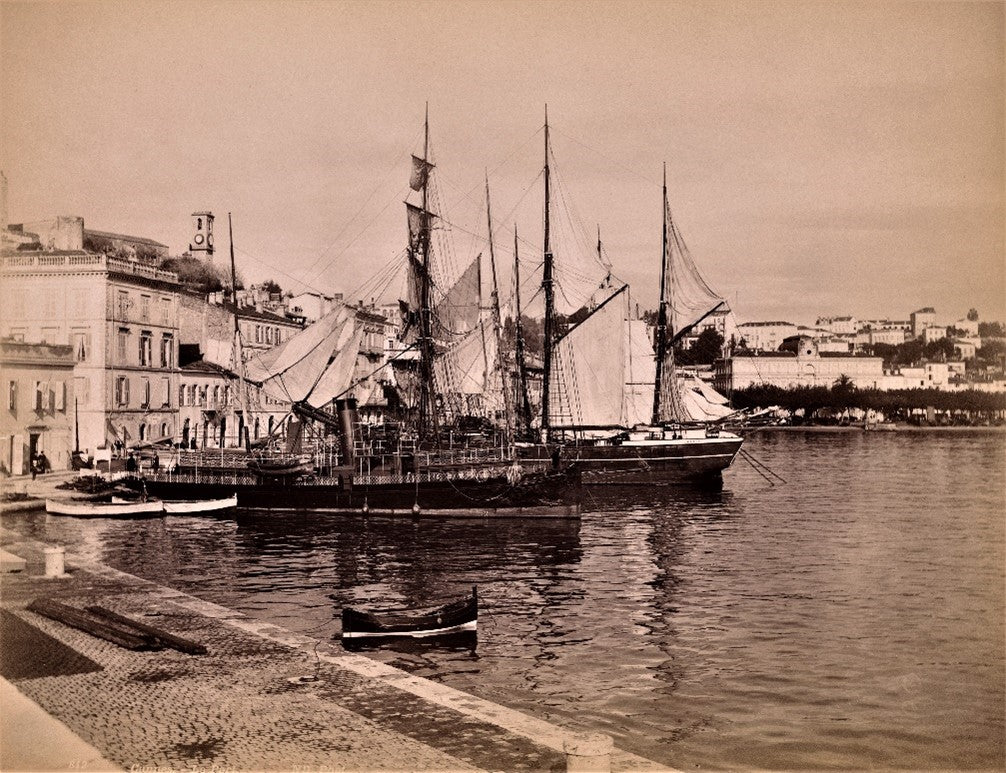 Sepia photograph of a European harbor with large sailing ships and traditional buildings, circa 1890