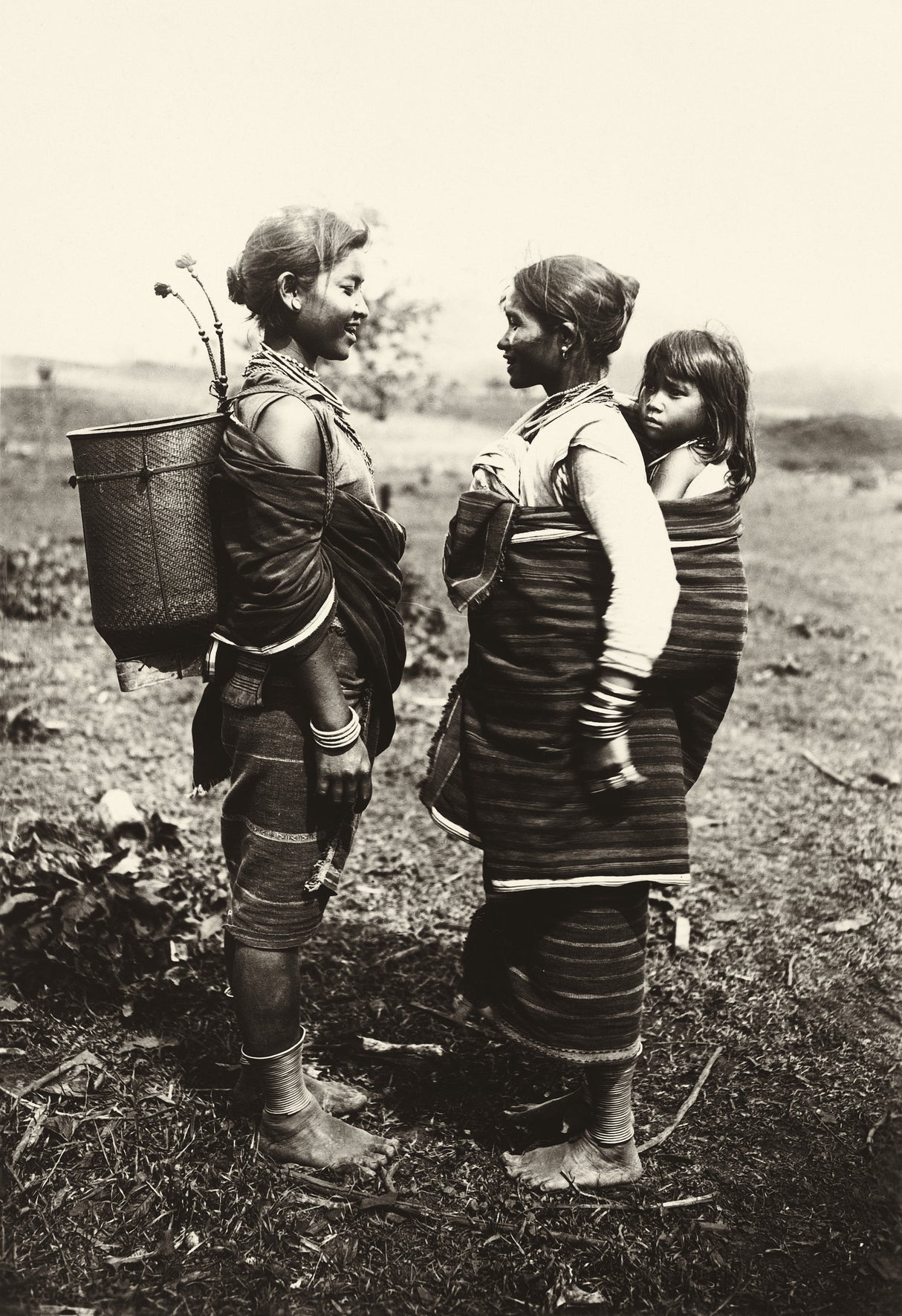 Sepia photograph of two indigenous highland women, one with a child on her back, in traditional wrap clothing