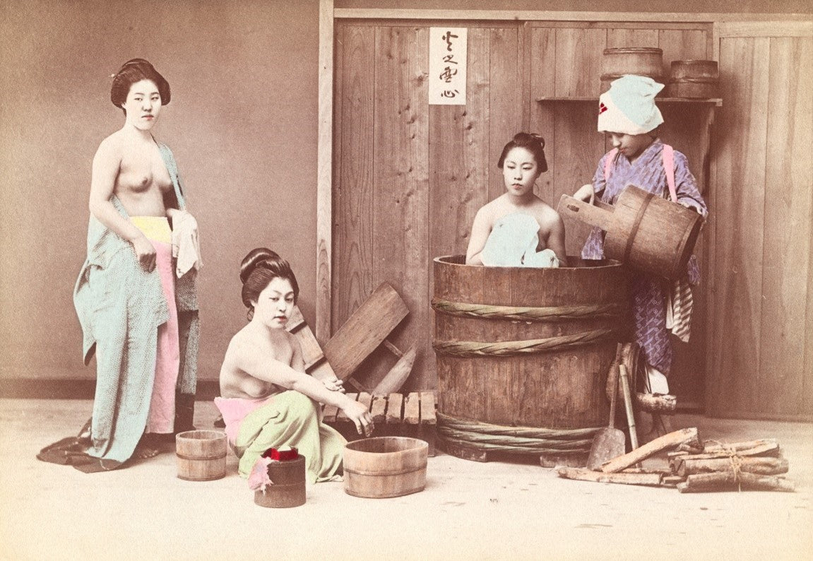 Hand-colored Meiji-era photograph of Japanese women bathing in a traditional sento, depicting daily life in 19th-century Japan.