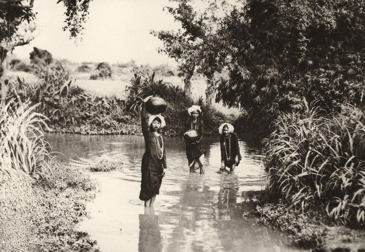 Sepia photo of three Southeast Asian women wading in a river with clay pots, surrounded by tropical foliage
