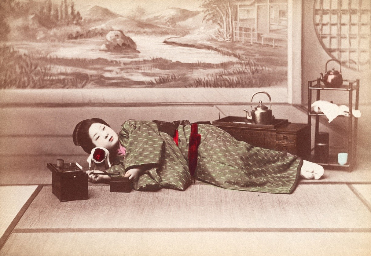 Hand-colored vintage photo of Japanese woman in green kimono smoking a pipe on tatami mat, with tea set in background