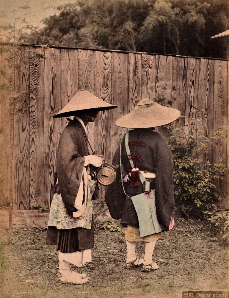 Hand-colored Meiji-era photograph of two Japanese Buddhist monks wearing traditional robes and straw hats, standing outdoors during pilgrimage.