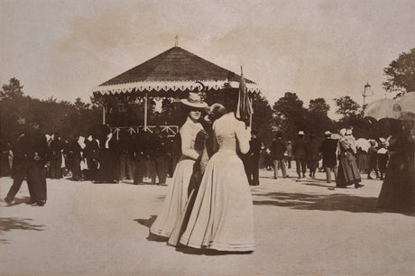 Sepia photo of two women in 19th-century dress near a bandstand in a park setting