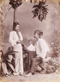 1890s studio portrait of a Burmese man seated and offering a betel nut to a standing woman, photographed by Philipp Klier.