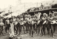 Archival photo of Dayak men drumming during a ceremony in front of a longhouse, central Borneo