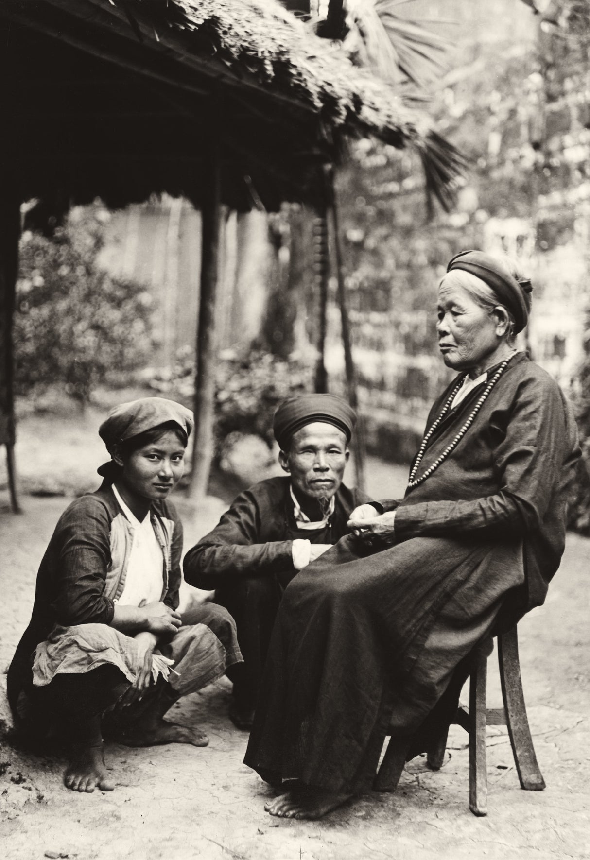 Black-and-white photo of an elder and two younger family members in a Vietnamese village, early 20th century
