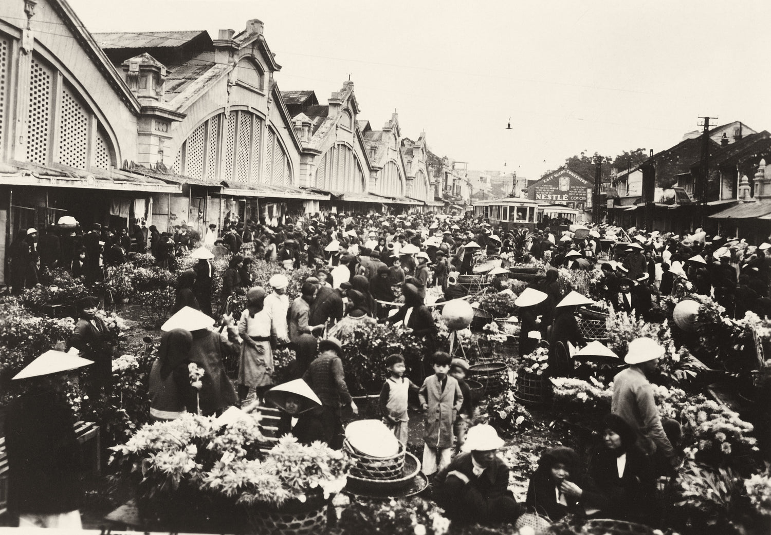 Historic black-and-white photo of Hanoi flower market with conical hats, French colonial arcades, and a tram, 1930s
