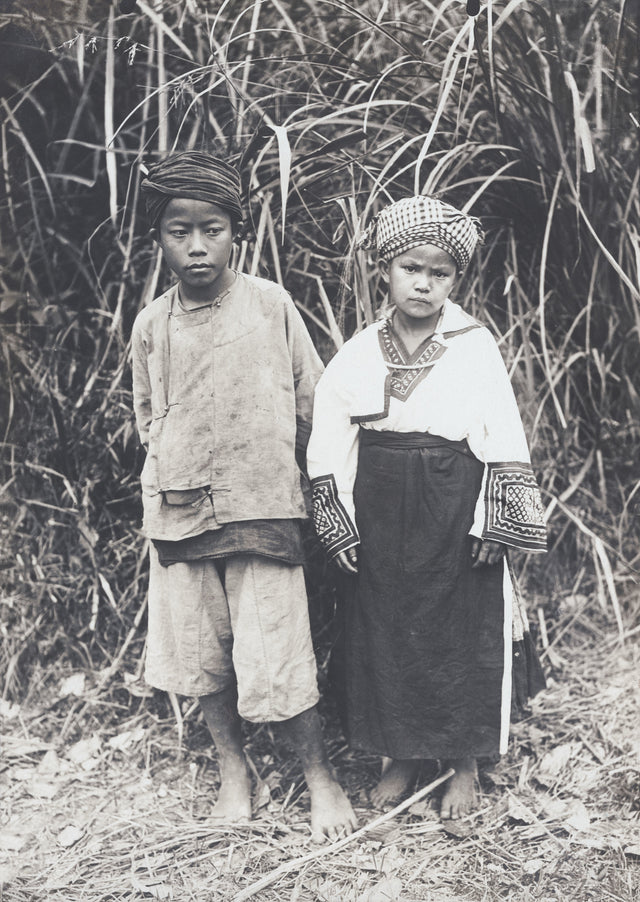 Young boy and girl in traditional highland dress, standing in jungle grass, Indochina, 1910s
