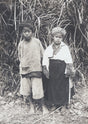 Young boy and girl in traditional highland dress, standing in jungle grass, Indochina, 1910s