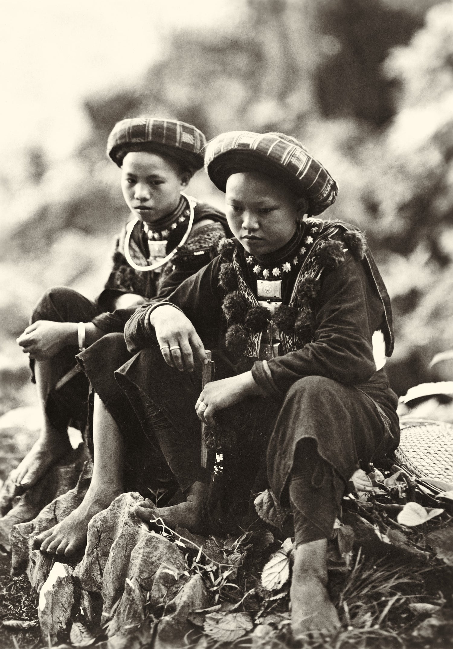 Sepia photograph of two highland women in traditional dress seated on rocks, Vietnam, 1930s