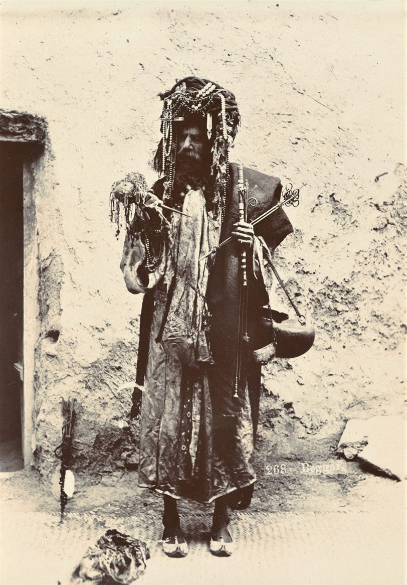 19th-century sepia photograph of a bearded man in layered clothing with ritual items, identified as a beggar or mystic