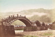 Hand-colored Meiji-era photograph of Kintai Bridge in Iwakuni, Japan, with figures crossing beneath its five arches and misty hills in the background.