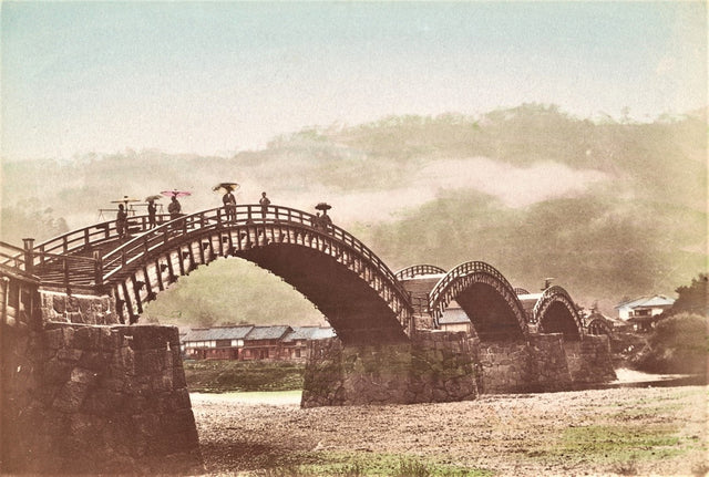 Hand-colored Meiji-era photograph of Kintai Bridge in Iwakuni, Japan, with figures crossing beneath its five arches and misty hills in the background.