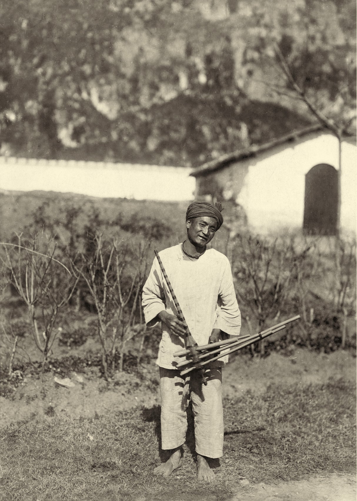 Man playing lusheng pipe instrument in a rural landscape, northern Indochina, 1910s