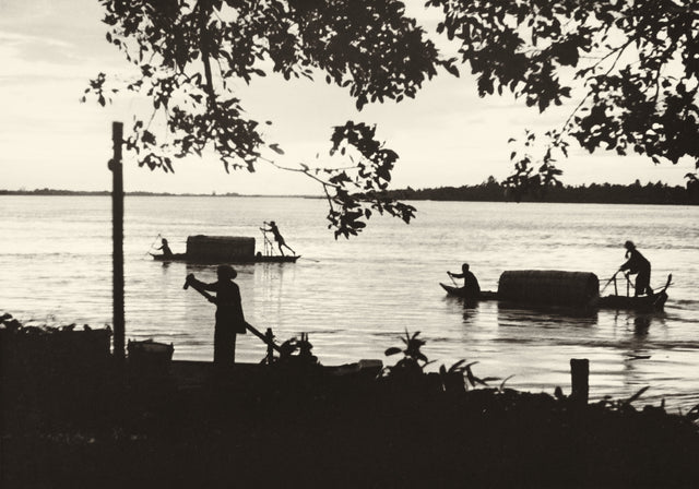 Sepia-toned photograph of bamboo rafts and boatmen on the Mekong River at dusk, circa 1920s–1930s