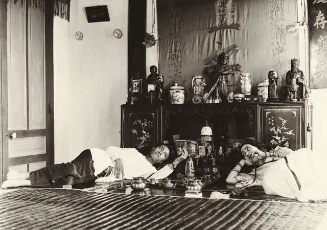 Sepia photograph of a man and woman reclining in an opium den, with ornate decor and Chinese-style furnishings