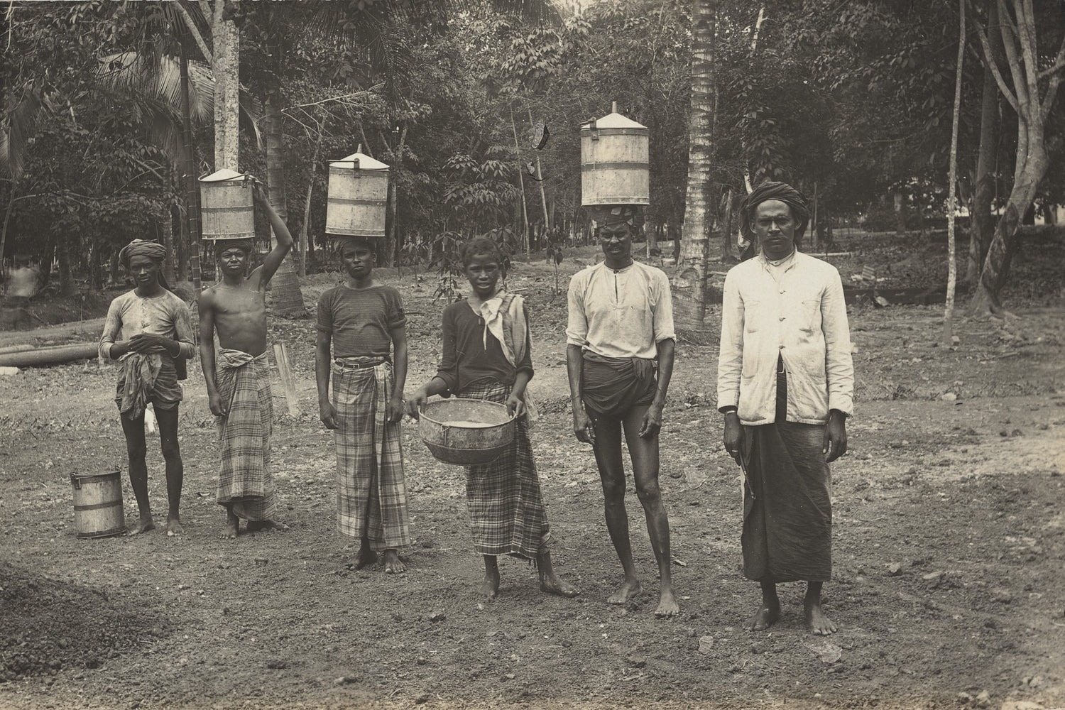 Black-and-white photo of rubber workers in Ceylon carrying latex vessels, early 20th century