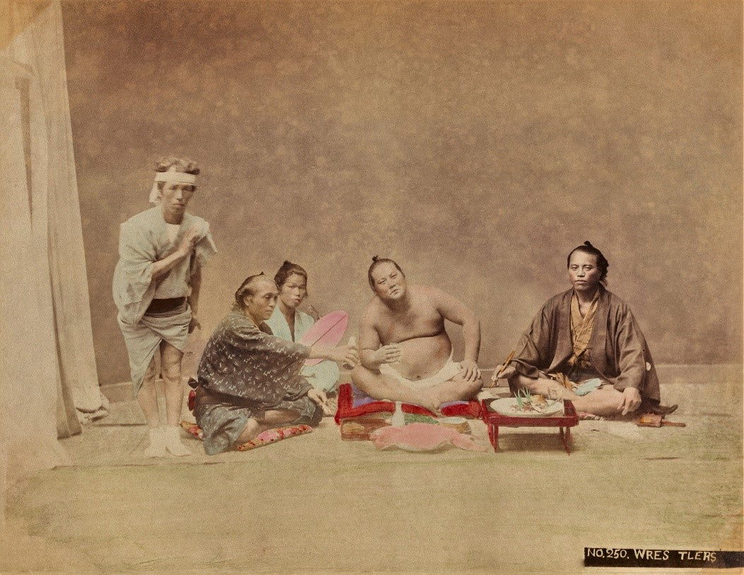 Meiji-era hand-colored photograph of sumo wrestler and attendants at a traditional Japanese dining scene