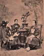 Sepia-toned 1901 studio portrait of three Chinese women in traditional silk garments seated around a tea table, engaging in a formal tea-drinking ritual in Hong Kong.