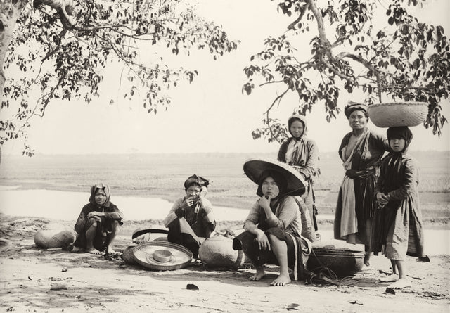 Sepia-toned photo of Vietnamese women vendors resting on a country road under trees, Tonkin, 1930s