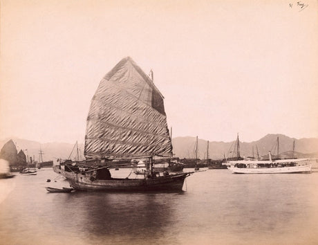 Sepia-toned 19th-century photograph of a traditional Chinese junk boat with a large sail in the harbor of Hong Kong, with distant mountains and other ships in view.
