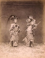 Historic sepia photograph of two Qing dynasty opera performers in elaborate embroidered costumes and ornate headdresses, staged in a studio setting.