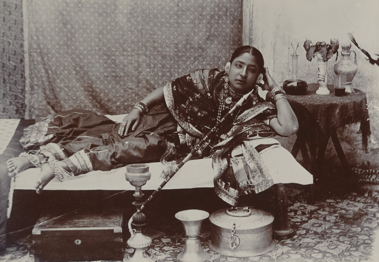 Sepia photograph of an Indian courtesan reclining with hookah and traditional jewelry, 1890s


