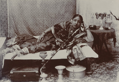 Sepia photograph of an Indian courtesan reclining with hookah and traditional jewelry, 1890s

