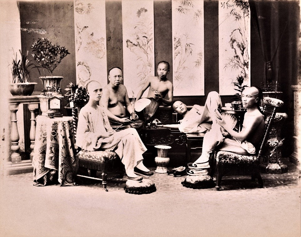 Sepia-toned photograph of Chinese men reclining and smoking in an ornate 19th-century opium den during the Qing Dynasty (1644–1912), surrounded by intricate furniture and decorative screens.