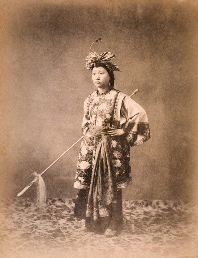 Sepia-toned studio portrait of a young Chinese opera performer in ornate traditional costume and headdress, holding a ceremonial horsehair whip, late Qing dynasty (1644–1912).