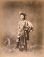 Sepia-toned studio portrait of a young Chinese opera performer in ornate traditional costume and headdress, holding a ceremonial horsehair whip, late Qing dynasty (1644–1912).